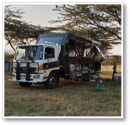 A group of people are standing in front of a large rock formation. A truck is parked nearby. AI generated content