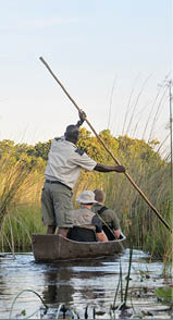 Tourists in a Mokoro, a wooden boat used in the Okavango Delta in Botswana with a park ranger peddling during sunset as part of a water safari