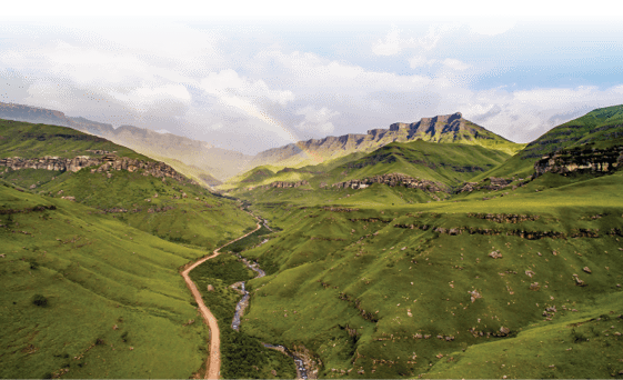 Fairy tale stunning rainbow over very wide valley called Sani Pass at South Africa and Lesotho border, with the offroad road and wild river and green meadows, with the rocks on the horizont