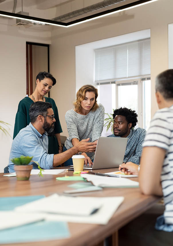 A group of people sitting around a table with a laptop. Description generated by AI