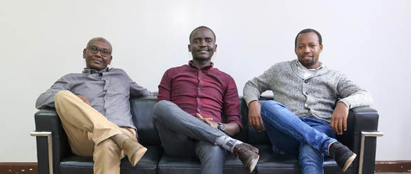 Three men sitting on a black couch. Description generated by AI