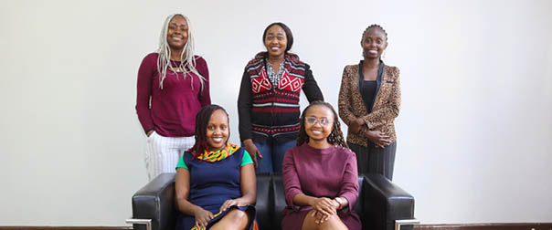 Five women sitting on a black couch. Description generated by AI