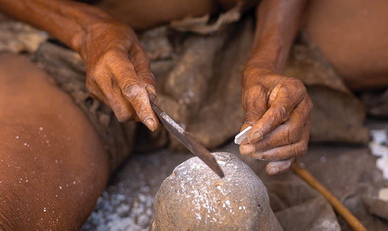 A person is shaping a rock with a knife. Description generated by AI