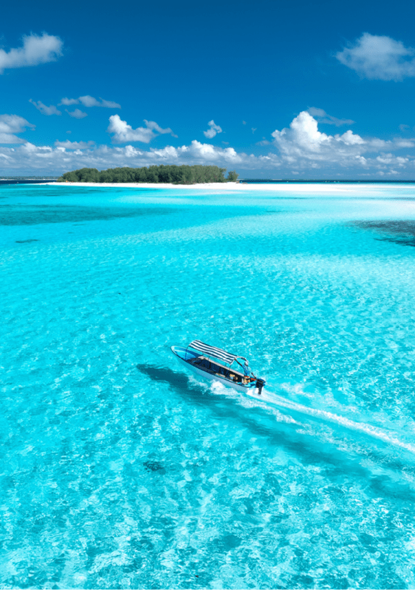 Aerial view of floating boat in transparent azure water on sunny summer day. Mnemba island, Zanzibar. Top view of yacht, sandbank in low tide, clear blue sea, sand, sky with clouds. Motorboat in ocean