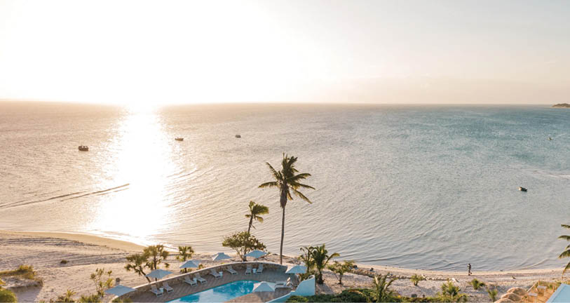A beautiful beach scene with a large body of water, palm trees, and a few boats. The sun is setting, casting a warm glow over the scene. AI generated content