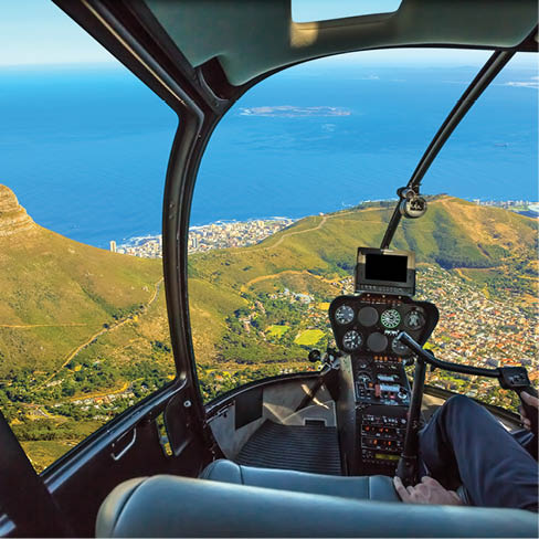 Helicopter cockpit flies in Lion's Head, coast and Cape Town in South Africa, with pilot arm and control board inside the cabin.