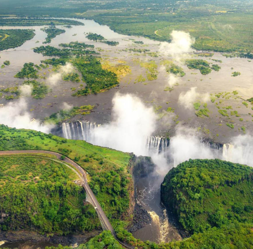 Victoria Falls in Zimbabwe and Zambia, Aerial helicopter photo, green forest around amazing majestic waterfalls of Africa. Livingston Bridge above the river