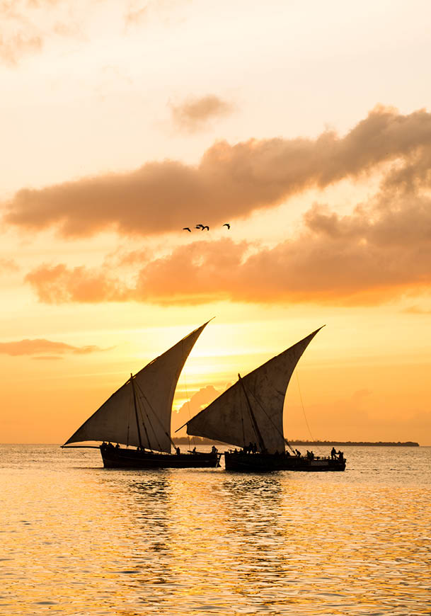 Two sailboats on the water with the sun setting in the background. Description generated by AI
