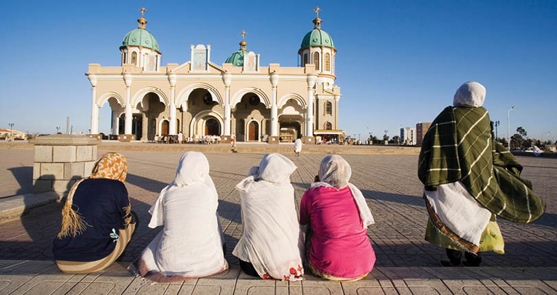 A group of people sitting on a sidewalk in front of a building. Description generated by AI