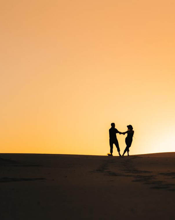 silhouettes of a happy young couple guy and girl on a background of orange sunset in the sand desert