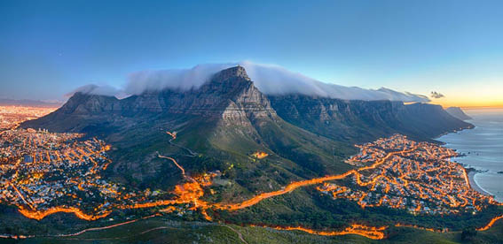 Table Mountain covered by its typical cloud table cloth and the twelve Apostles. Below on the left you can see Cape Town and the beautiful Camps Bay on the right. Taken right after sunset.