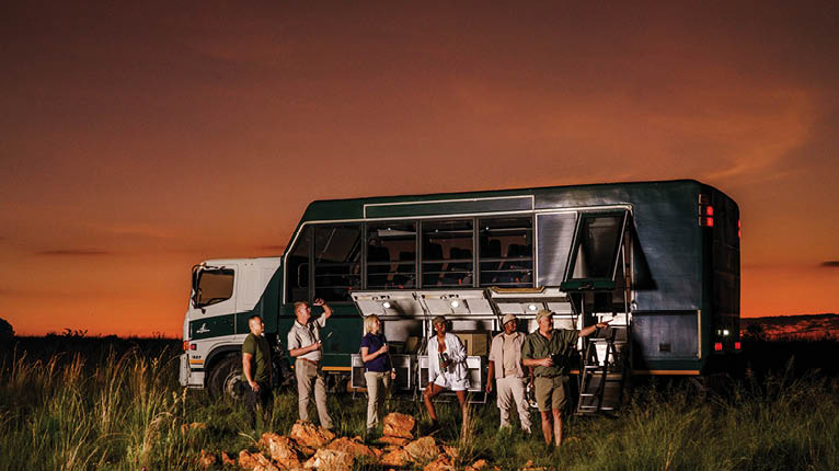 A group of people standing in front of a green and white truck. Description generated by AI