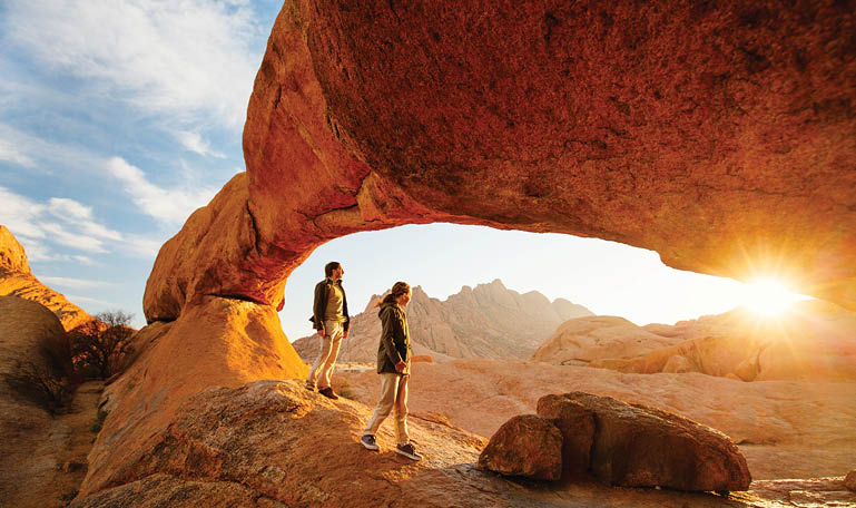 Two people walking under a rock formation. Description generated by AI