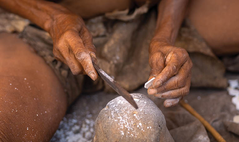 A person is shaping a rock with a knife. Description generated by AI