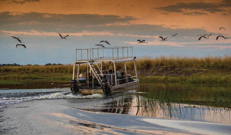 A boat with a group of people on it is traveling on a river. Description generated by AI