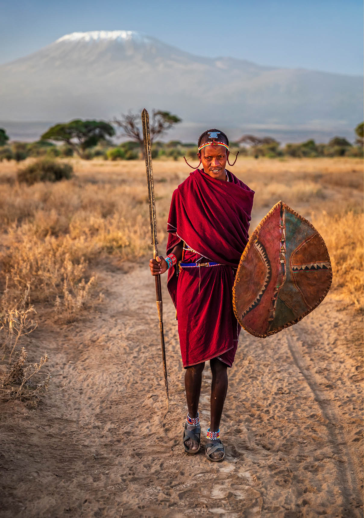 African warrior from Maasai tribe, Mount Kilimanjaro on the background, central Kenya, Africa. Maasai tribe inhabiting southern Kenya and northern Tanzania, and they are related to the Samburu.