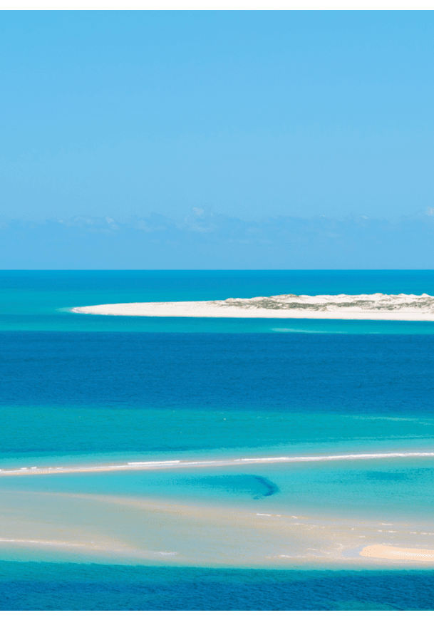 A beautiful blue ocean with a sandy beach and a mountain in the background. Description generated by AI