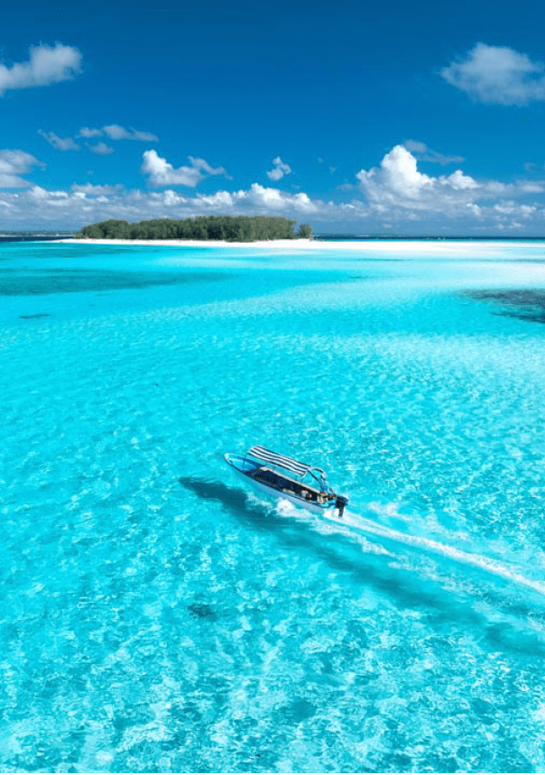 Aerial view of floating boat in transparent azure water on sunny summer day. Mnemba island, Zanzibar. Top view of yacht, sandbank in low tide, clear blue sea, sand, sky with clouds. Motorboat in ocean