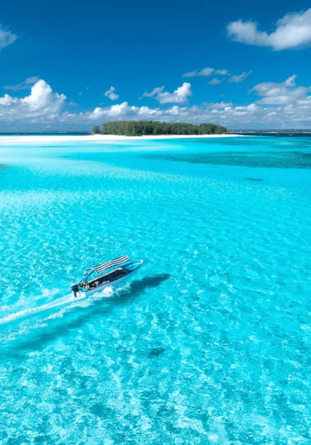 Aerial view of floating boat in transparent azure water on sunny summer day. Mnemba island, Zanzibar. Top view of yacht, sandbank in low tide, clear blue sea, sand, sky with clouds. Motorboat in ocean
